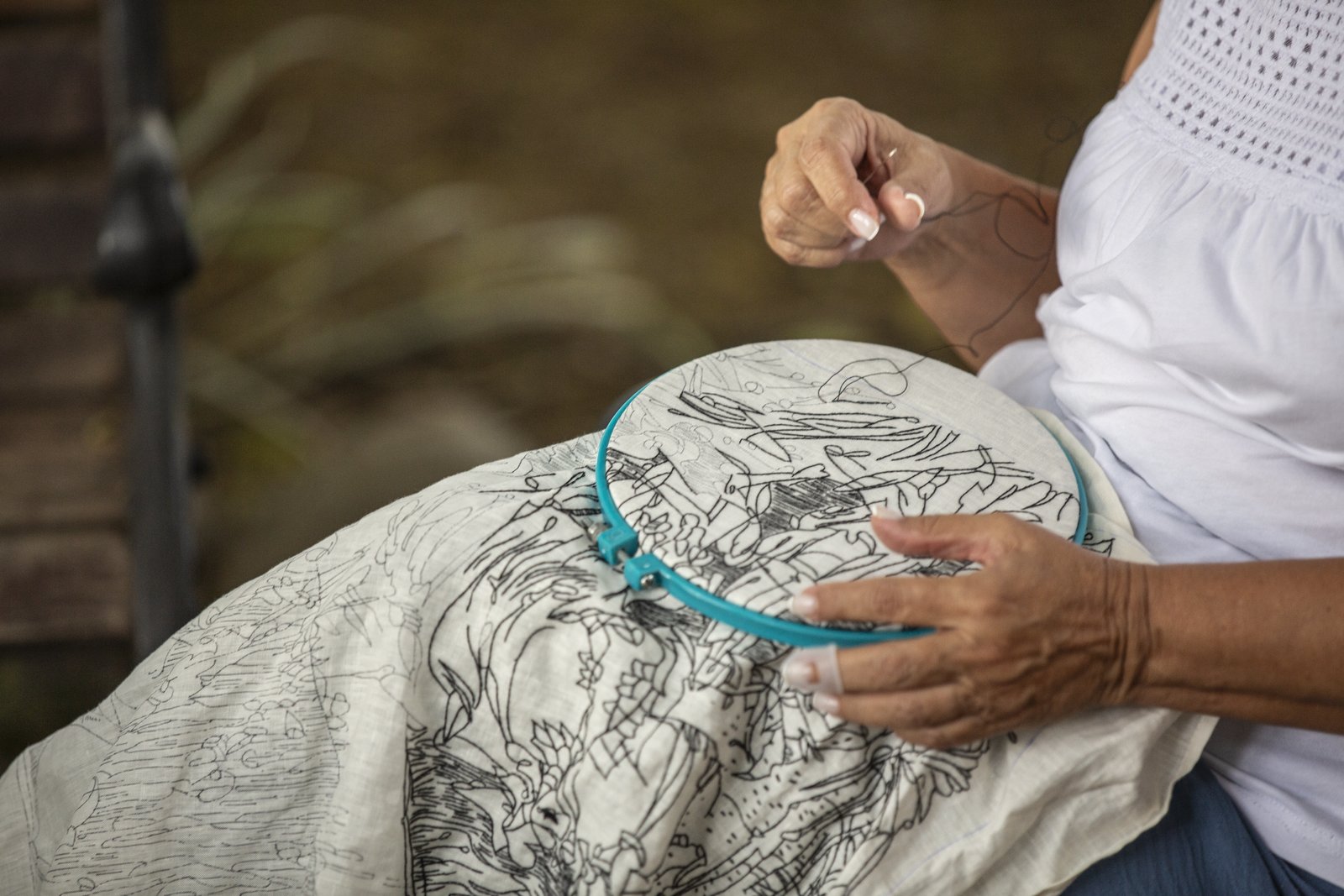 A hand mid-stitch, needle raised above the hoop
