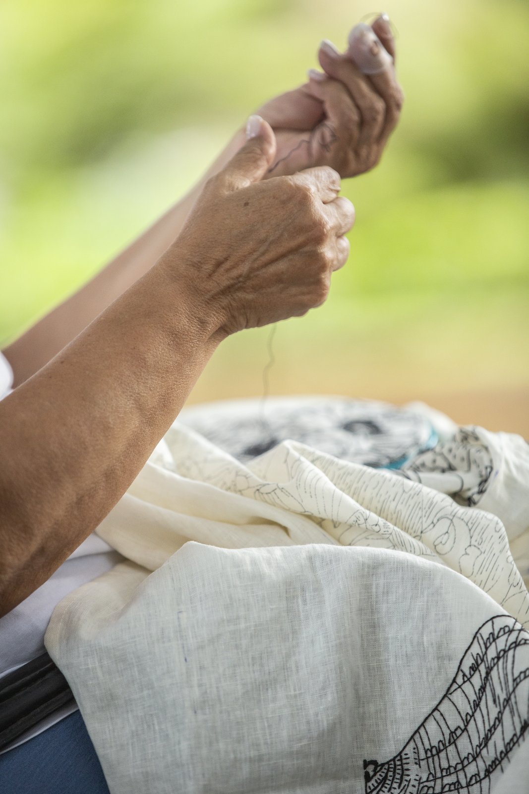 Hands threading a needle above folded linen